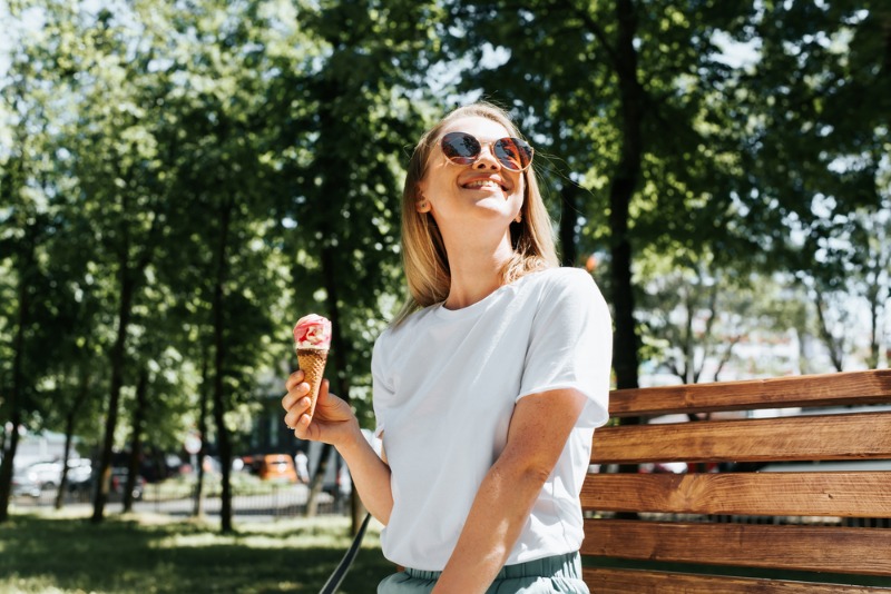 Estes Park Ice Cream: A young woman wearing sunglasses and holding and ice cream cone smiles during summer in Estes Park.